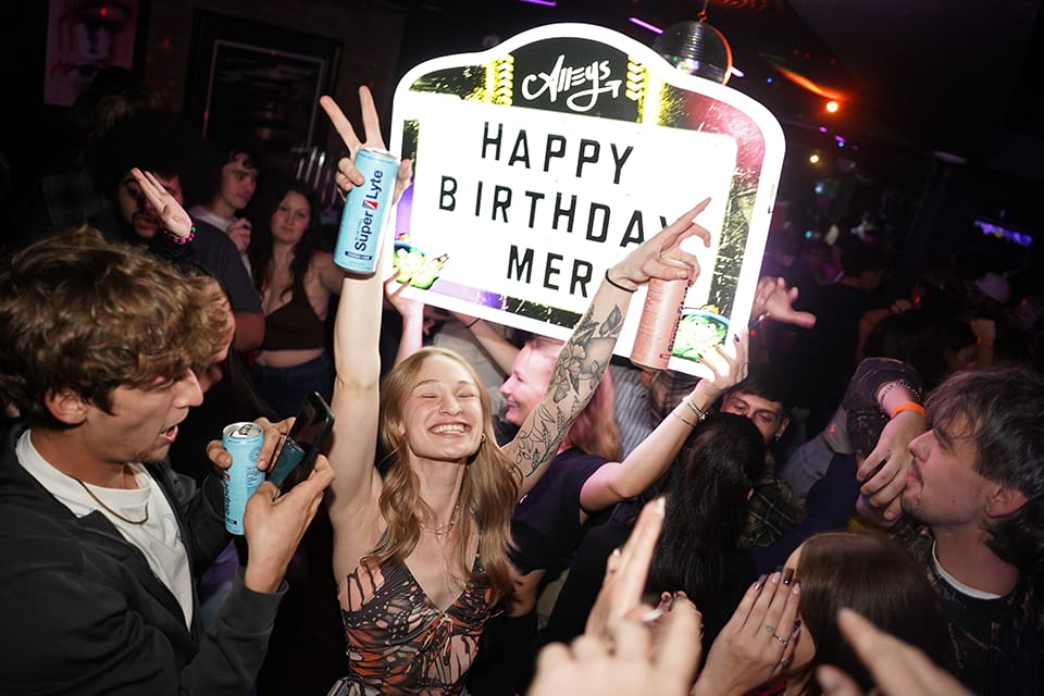 Birthday girl held up by the crowd under an Alleys happy birthday sign